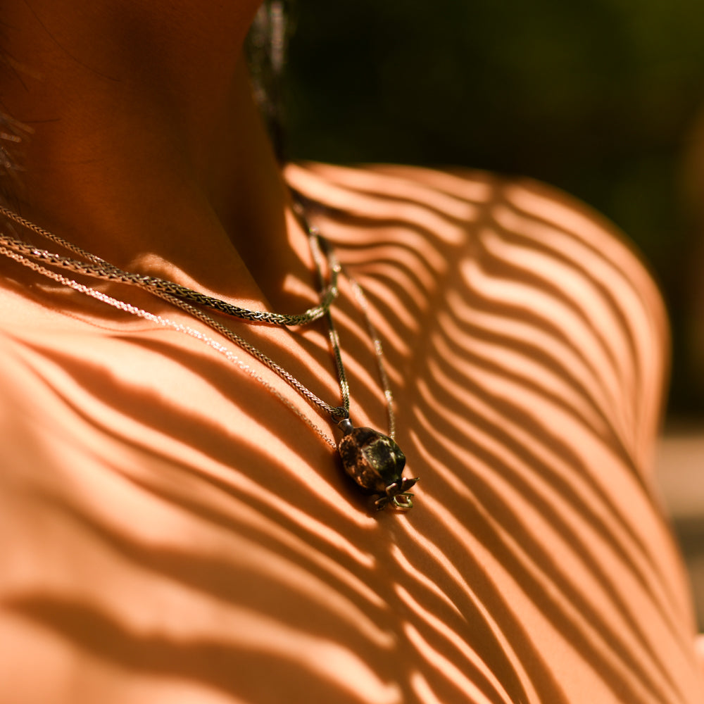 Poppy Seed Pendant on Womans Chest in the Forest with the Shadow of a fern cast over her